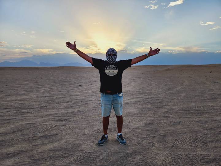 Silhouetted man with arms raised in a vast desert at sunset creating a dramatic sky glow