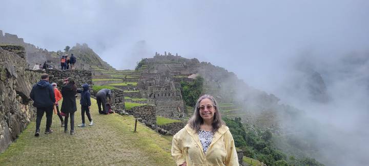 Visitor smiling in front of mist-shrouded terraces and stone ruins of Machu Picchu with other tourists nearby.