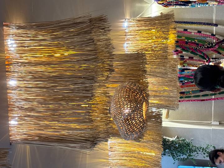 Interior shot of a restaurant ceiling decorated with hanging straw fringes and wicker lamp; back of a person visible.