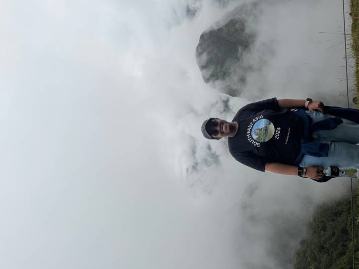 Traveller in a black cap smiling for the camera with cloud-shrouded Andean peaks behind