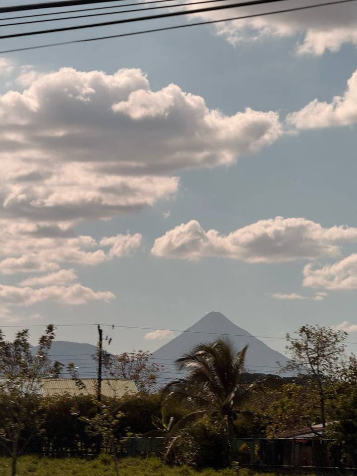 Distant volcanic peak rising above a layer of drifting clouds on a hazy afternoon