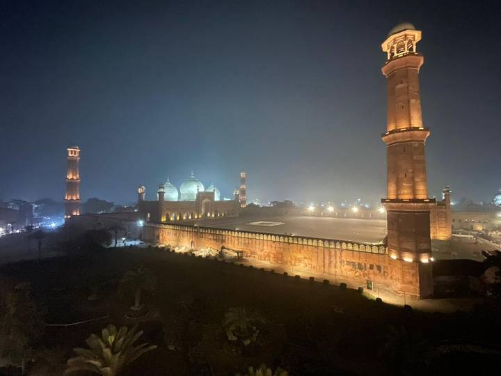 The illuminated Badshahi Mosque and its soaring minarets glow against the Lahore night sky.