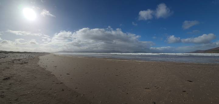 Wide sandy beach in Ireland with dramatic clouds, distant mountains and bright low sun