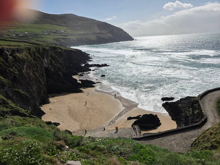 Rugged Irish coastline with sandy cove, cliffs and a winding path with a few visitors on the beach