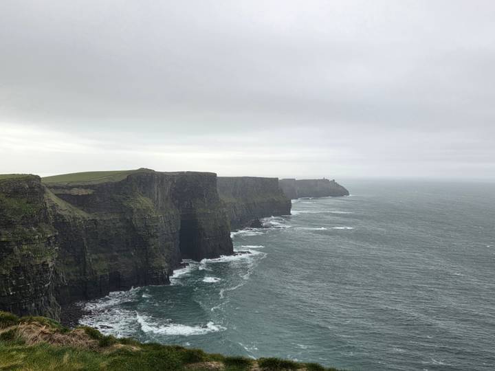Dramatic view of the sheer Cliffs of Moher stretching into a misty horizon above rough Atlantic waters