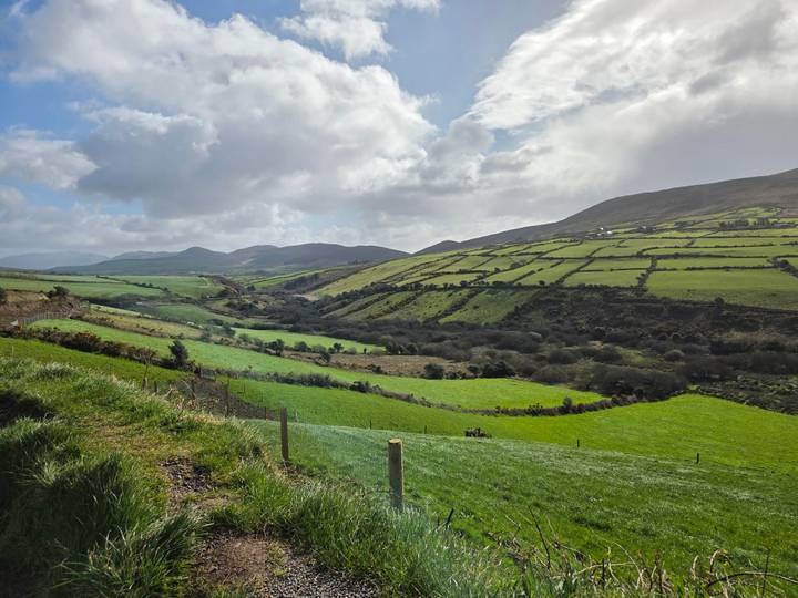 Patchwork of vivid green fields and rolling hills under dramatic clouds on Ireland's scenic peninsula