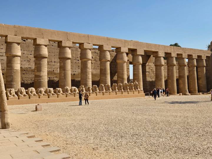 Row of ram-headed sphinx statues and tall stone columns inside Luxor Temple complex