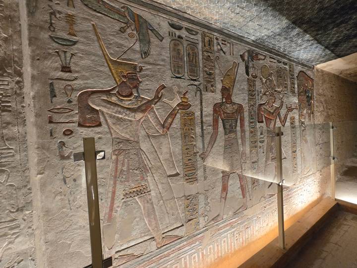 Colorful painted wall relief of ancient Egyptian figures holding objects with hieroglyphs all around