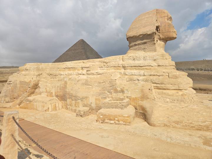 Side profile of the Great Sphinx with the Pyramid of Khafre behind under partly cloudy skies