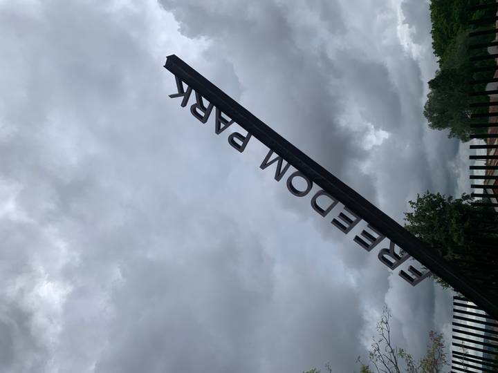 Angled metal sign reading FREEDOM PARK against a backdrop of brooding grey clouds