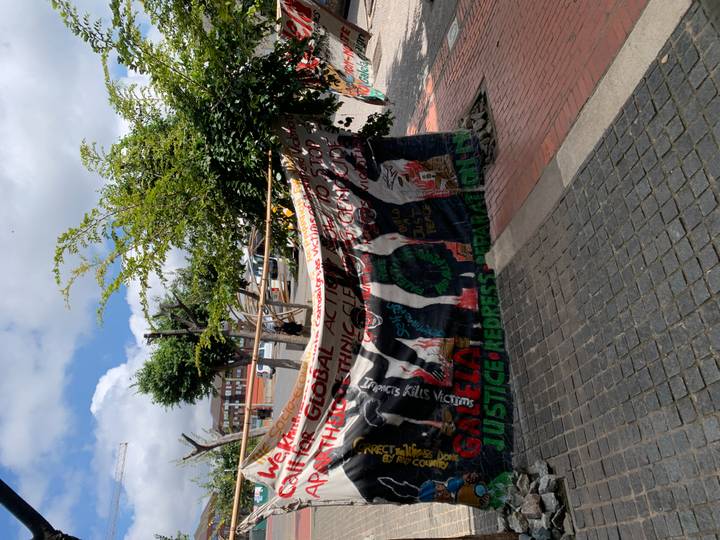 Colorful protest banner about global activism hanging between street trees on a city pavement