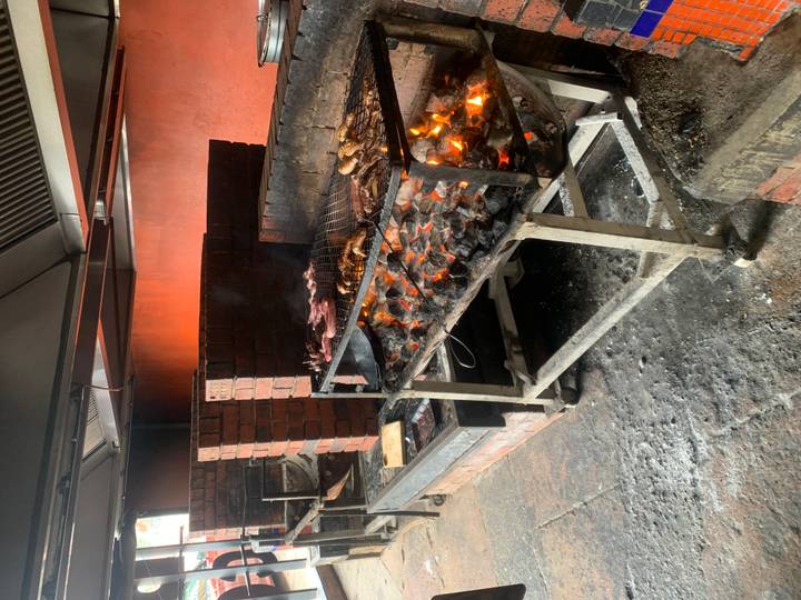 Indoor brick barbecue with glowing coals grilling various cuts of meat.
