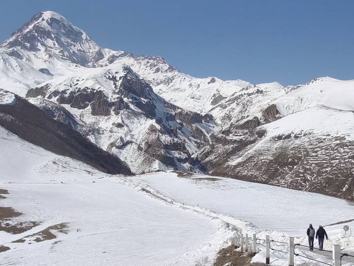 Snow-covered peaks and rugged valleys of the Caucasus under a clear blue sky.