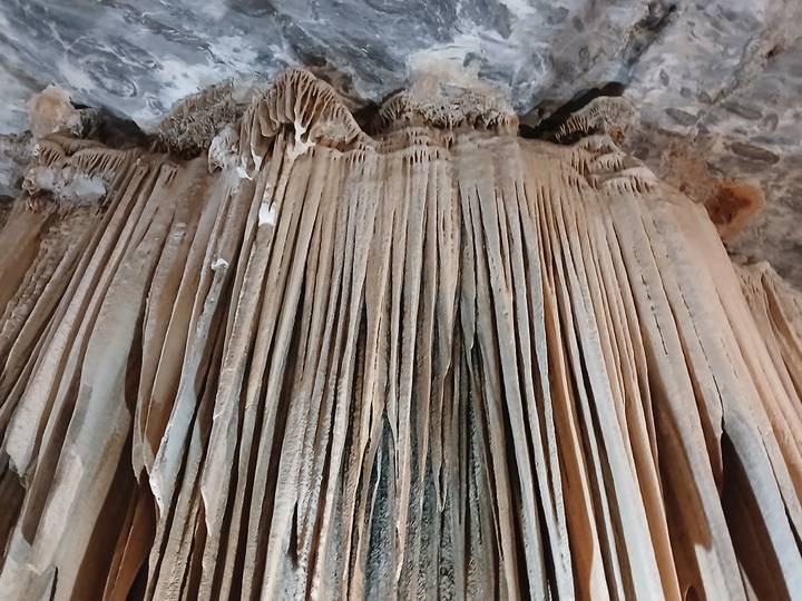 Massive curtain-like limestone stalactites hanging inside a cave chamber.