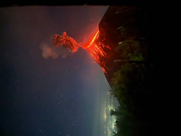 Nighttime eruption of a volcano sending glowing lava and ash plumes under starry sky