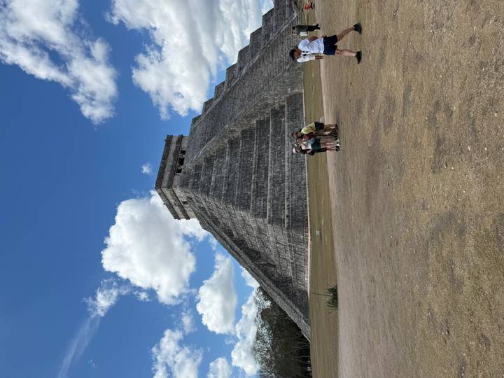 Iconic pyramid of Chichen Itza rising against a blue sky with tourists at its base