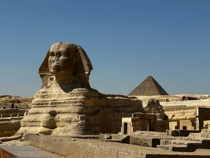 Majestic Sphinx profile with a pyramid rising behind under a clear blue Egyptian sky.