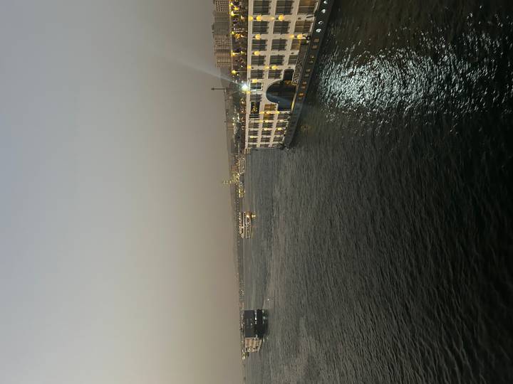 River cruisers glide along a wide stretch of the Nile at dusk beneath a hazy sky.
