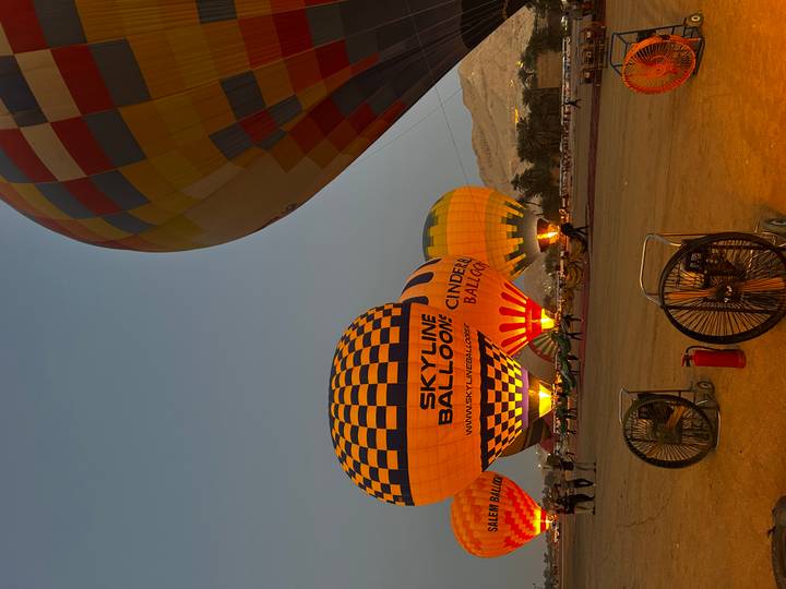 Inflated hot-air balloons glow with burner flames on a desert launch field at dawn.