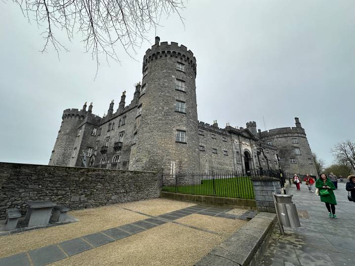 Imposing grey-stone Kilkenny Castle towers above visitors on a cloudy day.