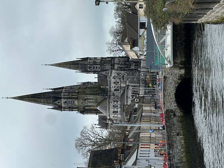 Twin-spired St Fin Barre's Cathedral dominates the riverfront streetscape on a grey day.