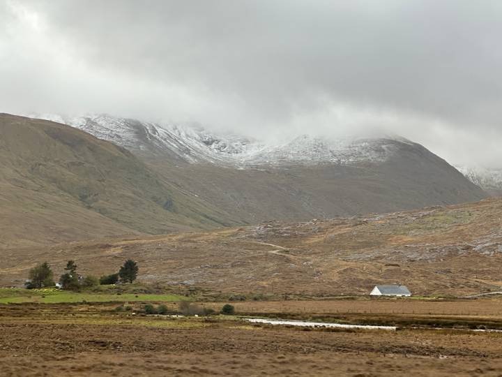 Misty, snow-dusted mountains loom over a lonely cottage in the rolling Connemara landscape.