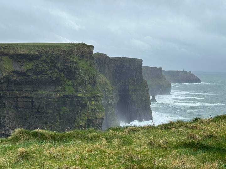 Sheer green-streaked cliffs of Moher plunge into crashing Atlantic waves under stormy skies.