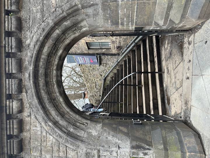 Stone archway frames steep steps leading to a historic churchyard, with a visitor ascending.