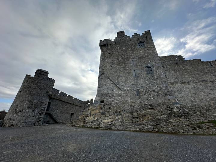 Massive grey stone fortress perches on rugged bedrock beneath a moody sky.