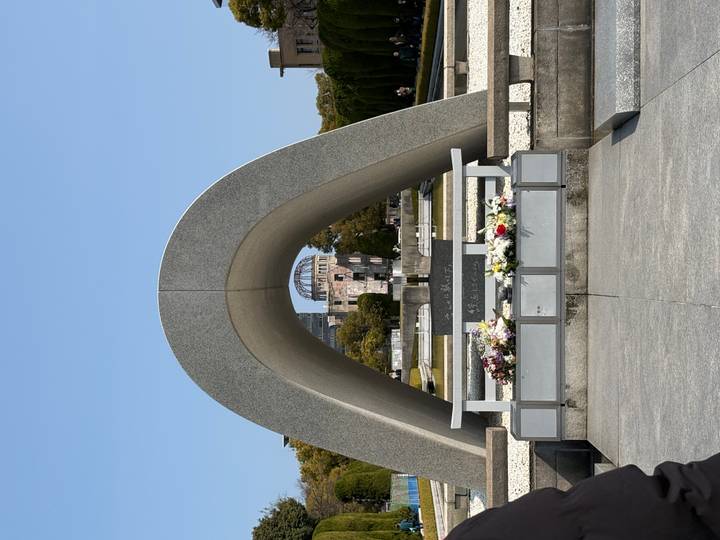 Stone arch cenotaph framing the Atomic Bomb Dome across a reflecting pond in Hiroshima Peace Memorial Park.