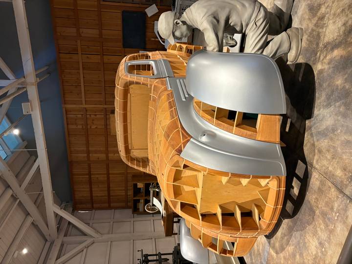 Wooden frame of a classic automobile under construction displayed in a workshop museum setting.