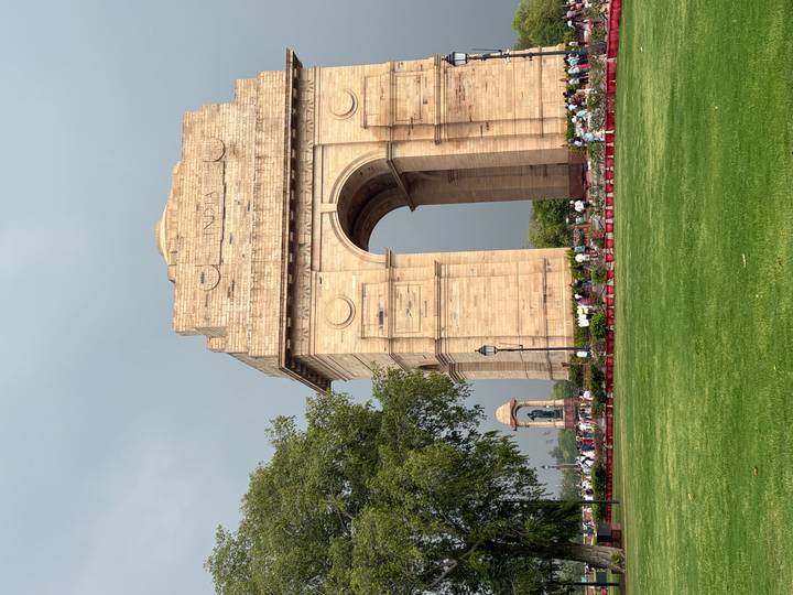 Stone India Gate war memorial rises over a green lawn against an overcast sky.