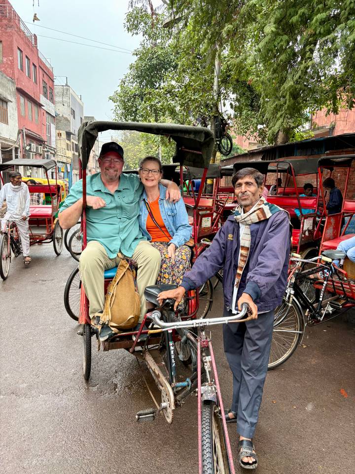 Tourists ride a cycle rickshaw through a bustling narrow street lined with more rickshaws.