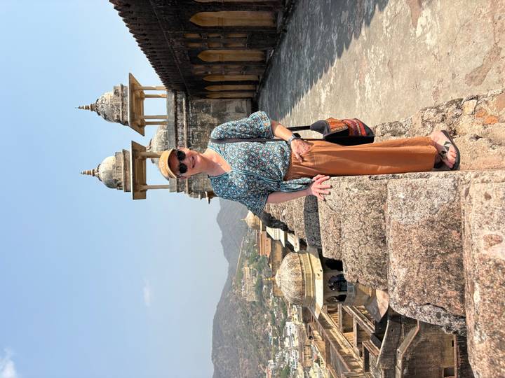 Traveller poses on the ramparts of Amber Fort overlooking arid hills and domed pavilions.