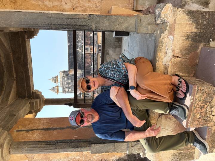 Couple rests on a stone bench inside a historic fort pavilion with domes in background.