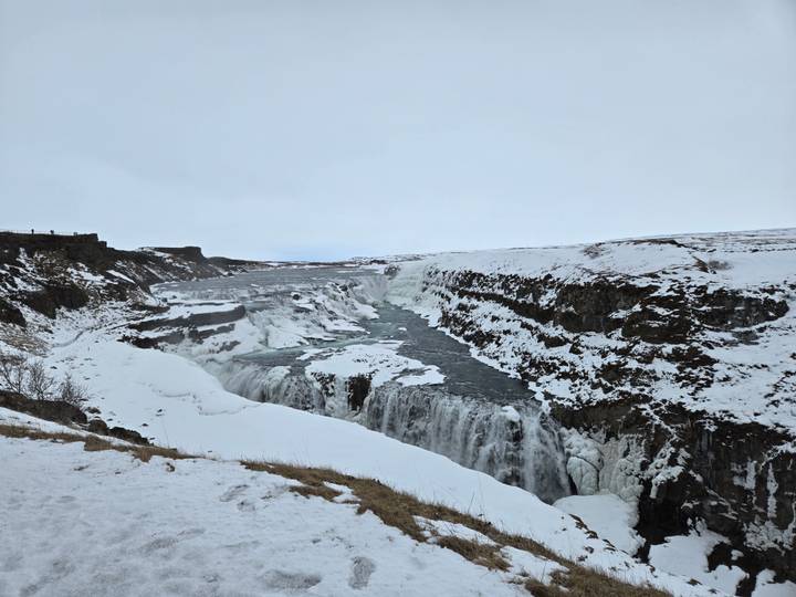 Partially frozen Gullfoss waterfall thunders through icy canyon on overcast winter day