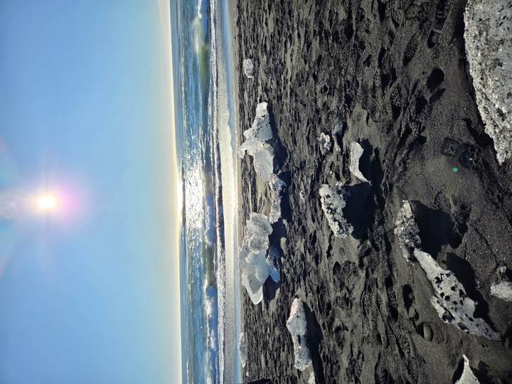 Glittering ice fragments sparkle on black sand at Iceland's Diamond Beach under bright sun
