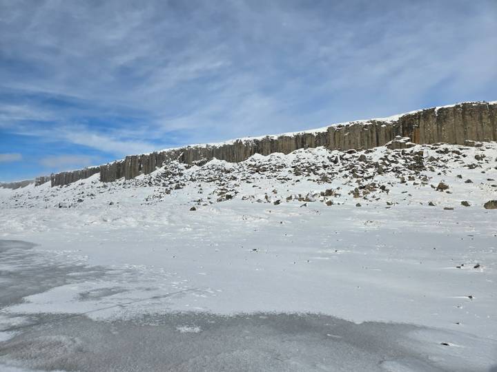 Rows of basalt columns rim a snowy Icelandic plateau beneath a blue sky