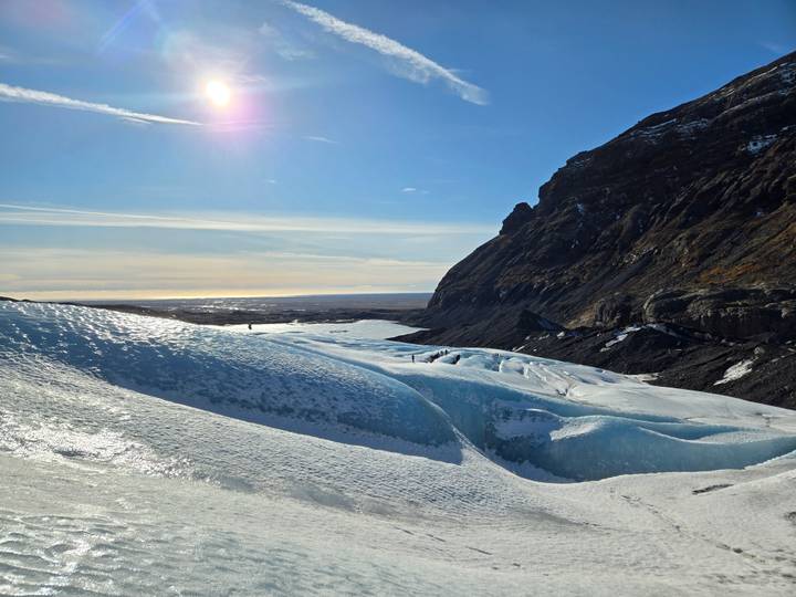 Blue glacial ice formations stretch toward distant ocean beneath rugged mountains