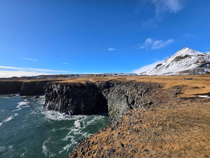Jagged sea cliffs and teal waters meet snowy peaks near Arnarstapi coastline