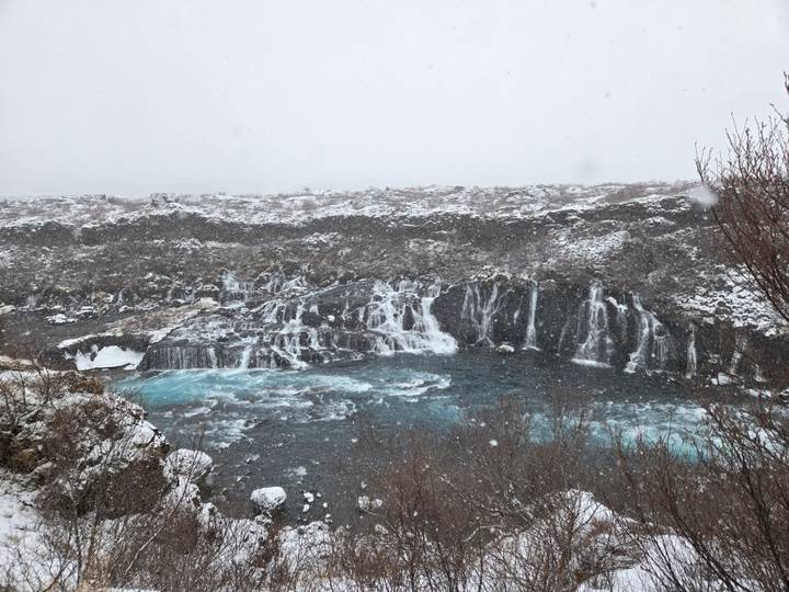 Snowy landscape with cascading Hraunfossar-style waterfalls into icy blue pool