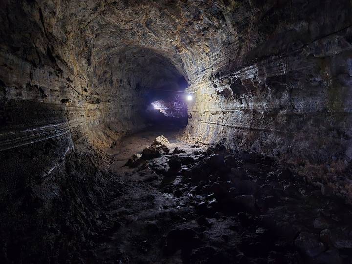 Dimly lit lava tunnel with rough rock walls and a single lamp illuminating the path.