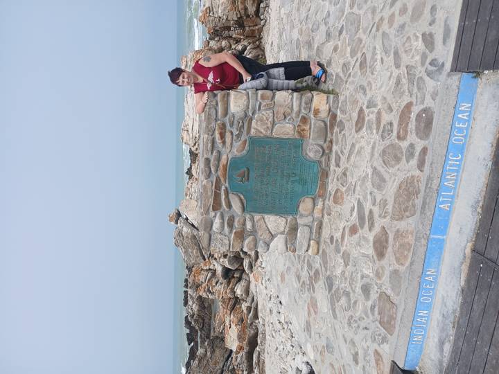 Traveller poses beside the Southern Tip of Africa monument at Cape Agulhas where two oceans meet.