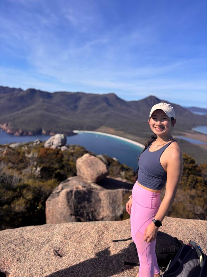 Smiling hiker enjoys a panoramic view of Wineglass Bay and surrounding mountains in Tasmania.