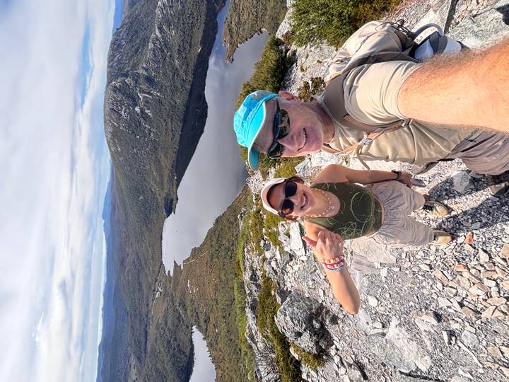 Couple smiles for a selfie overlooking a serene alpine lake and rolling Tasmanian highlands.