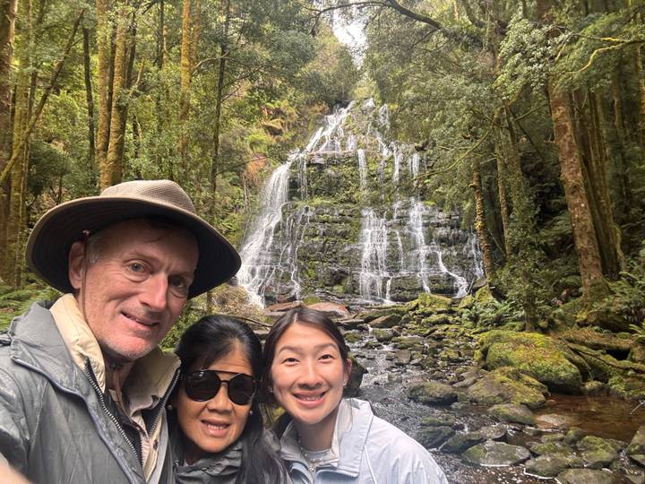 Family poses in front of a cascading rainforest waterfall surrounded by mossy rocks and trees.