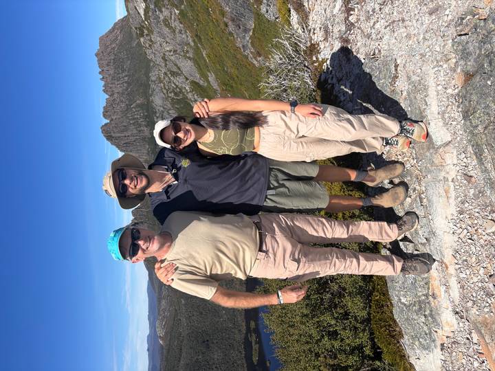 Guide stands with two travellers on a lookout with rugged Cradle Mountain peaks behind.