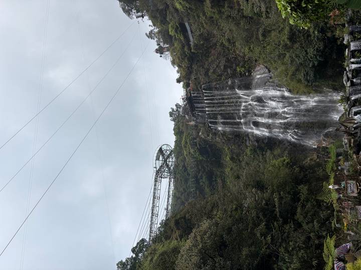 Tall waterfall cascading down cliff with sightseeing walkway and coaster track above