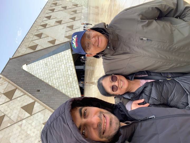 Three travelers smile in a selfie outside the modern triangular entrance of Cairo’s Grand Egyptian Museum.