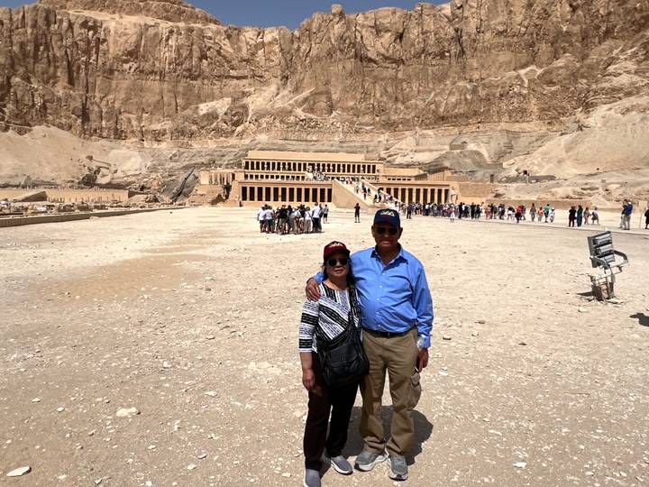 Couple stands in the open square facing the terraced Mortuary Temple of Hatshepsut in the Theban cliffs.